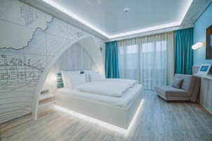 Un dormitorio moderno con una cama grande, un espacio para sentarse y un mural original en la pared.