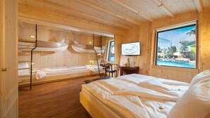 A wooden cabin room with bunk beds, a desk, and a large window overlooking a pool. - Hotel Victory Therme Erding (Erding)