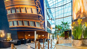 A lobby with a curved blue and gold facade, a glass ceiling, and a seating area with sofas and a coffee table. - Hotel Victory Therme Erding (Erding)