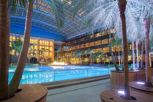 Un vestíbulo de hotel con piscina, palmeras y techo de cristal.