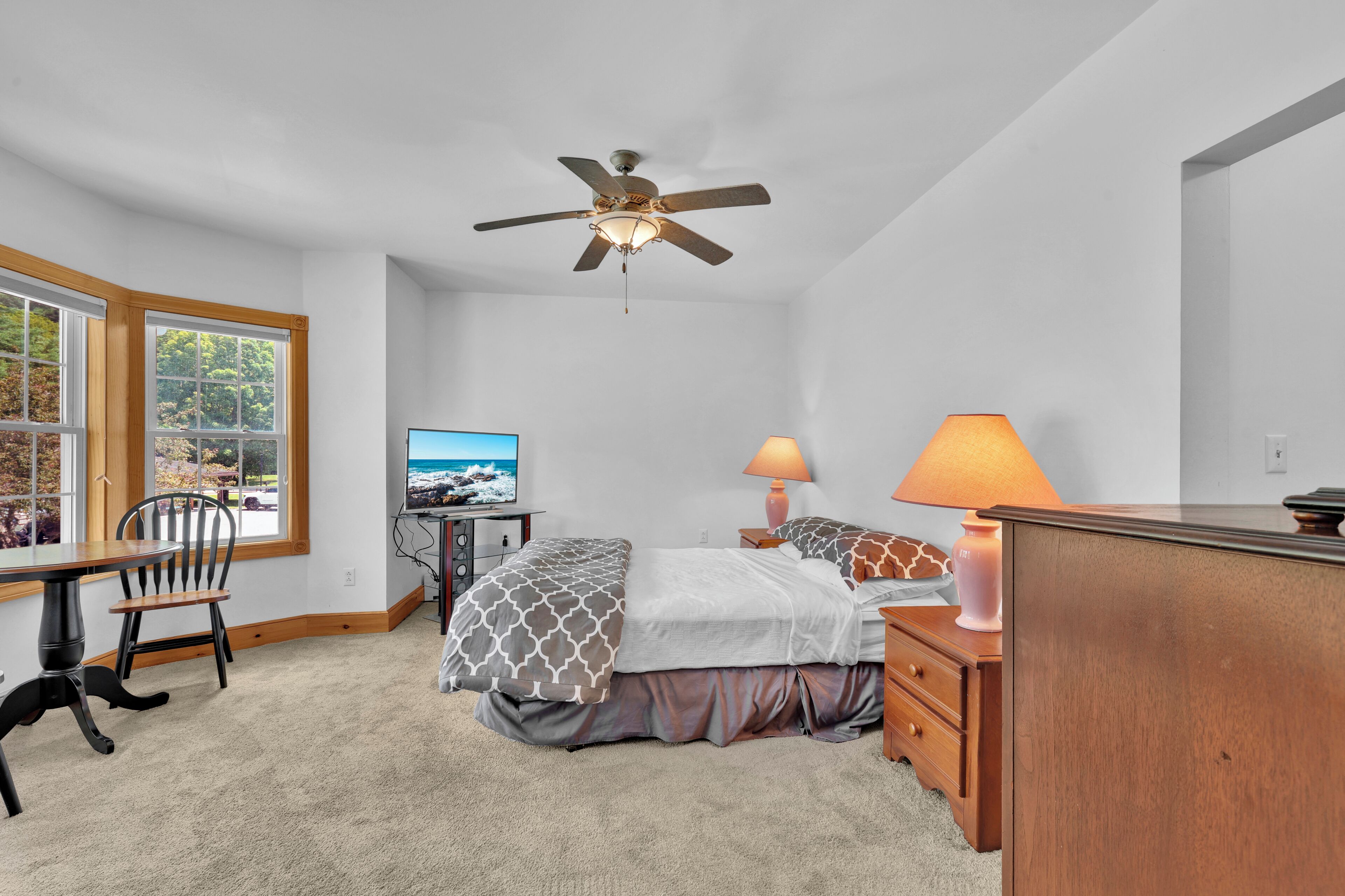 A bedroom with a bed, a desk, a chair, a television, and a ceiling fan.