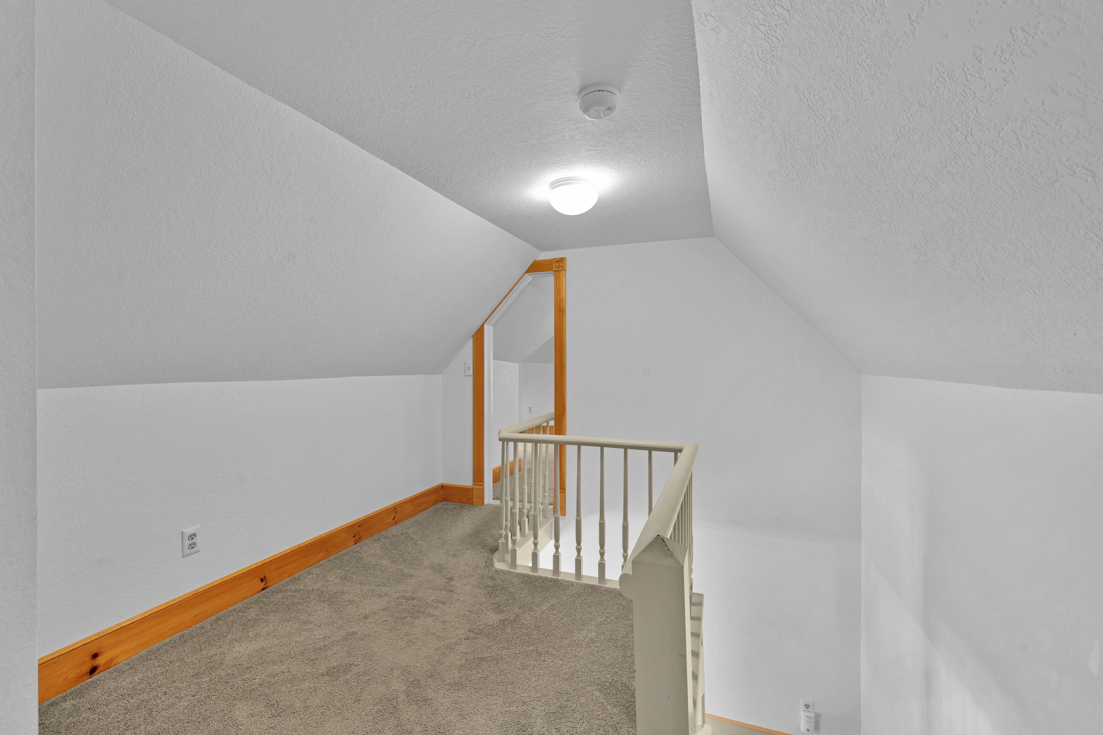 A room with a sloped ceiling, a wooden staircase, and a carpeted floor.