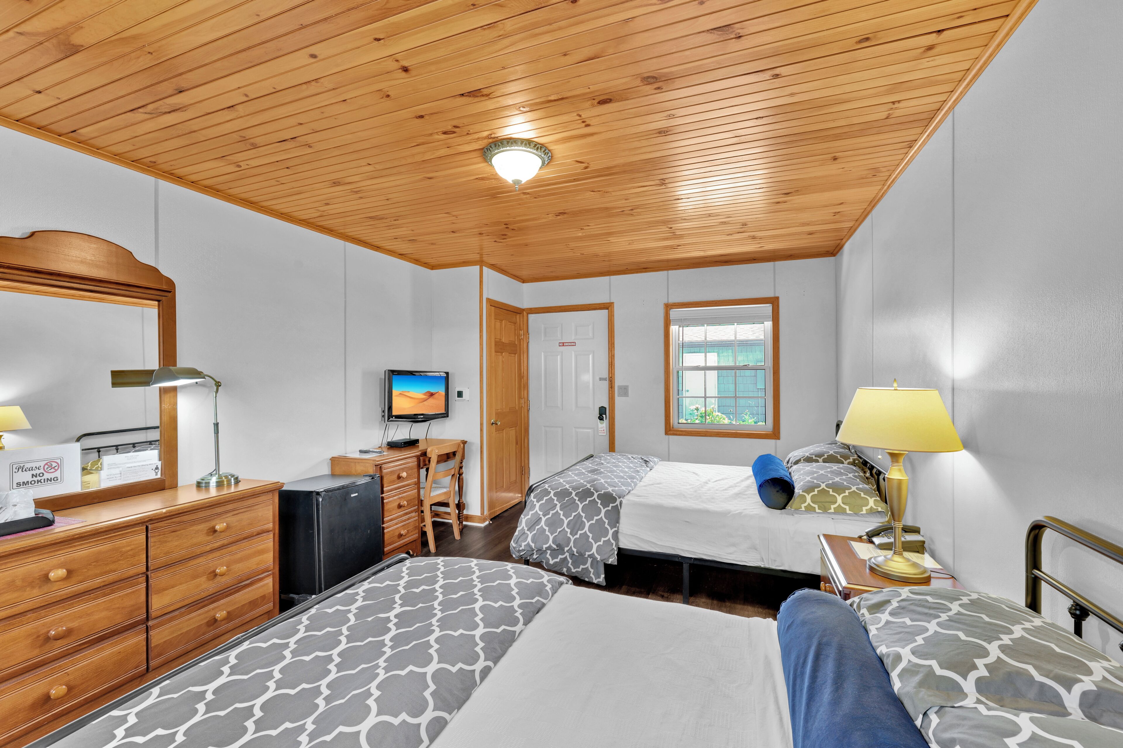 A hotel room with two beds, a desk, a television, and a window.