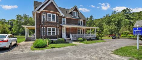 A two-story house with a porch and a driveway leading to a parking area.