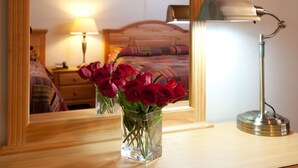 A mirror reflecting a bed, a bedside lamp, and a vase with red roses on a wooden dresser. - Blue Hill Lodge (Claryville)