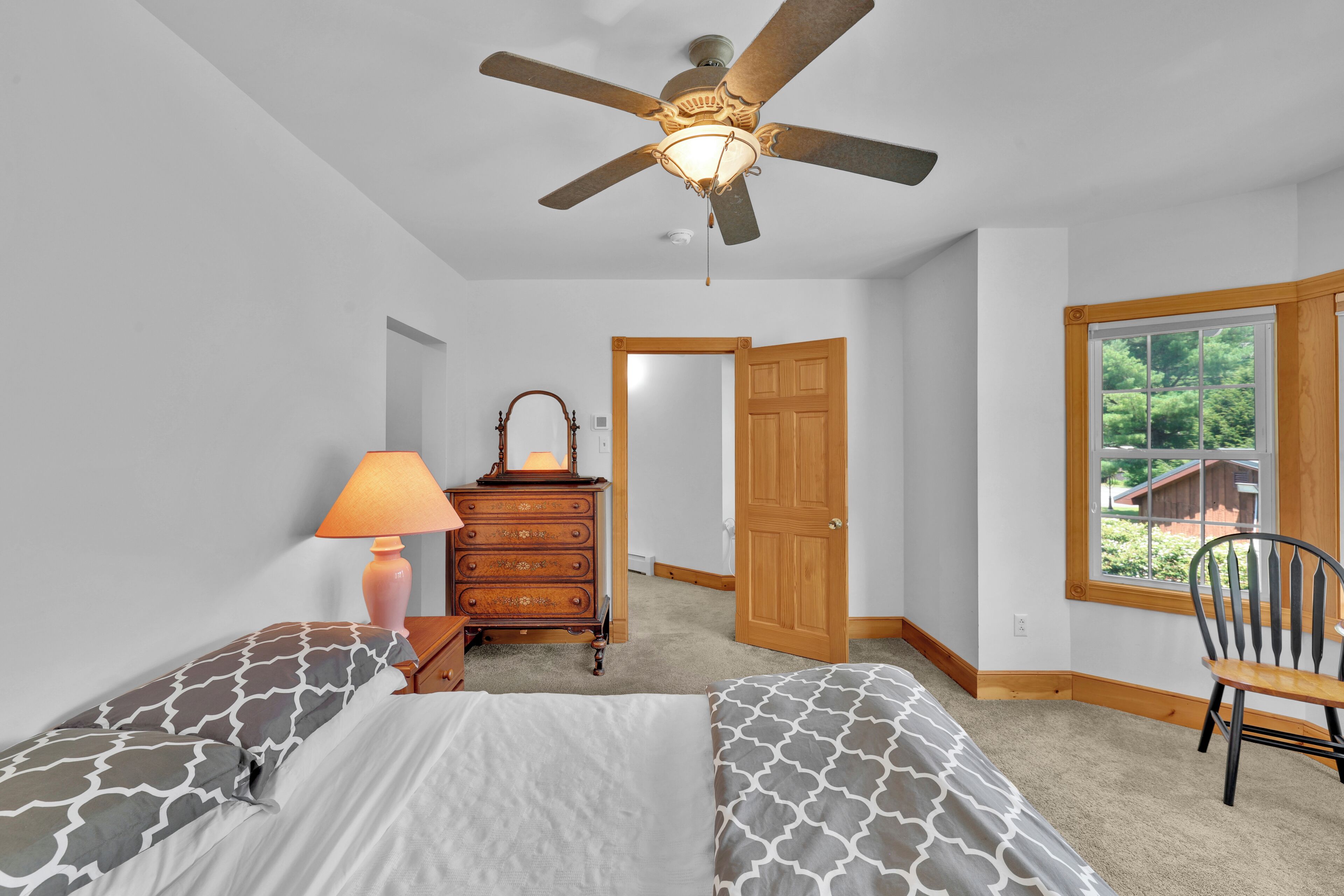 A bedroom with two beds, a dresser, a lamp, and a ceiling fan.