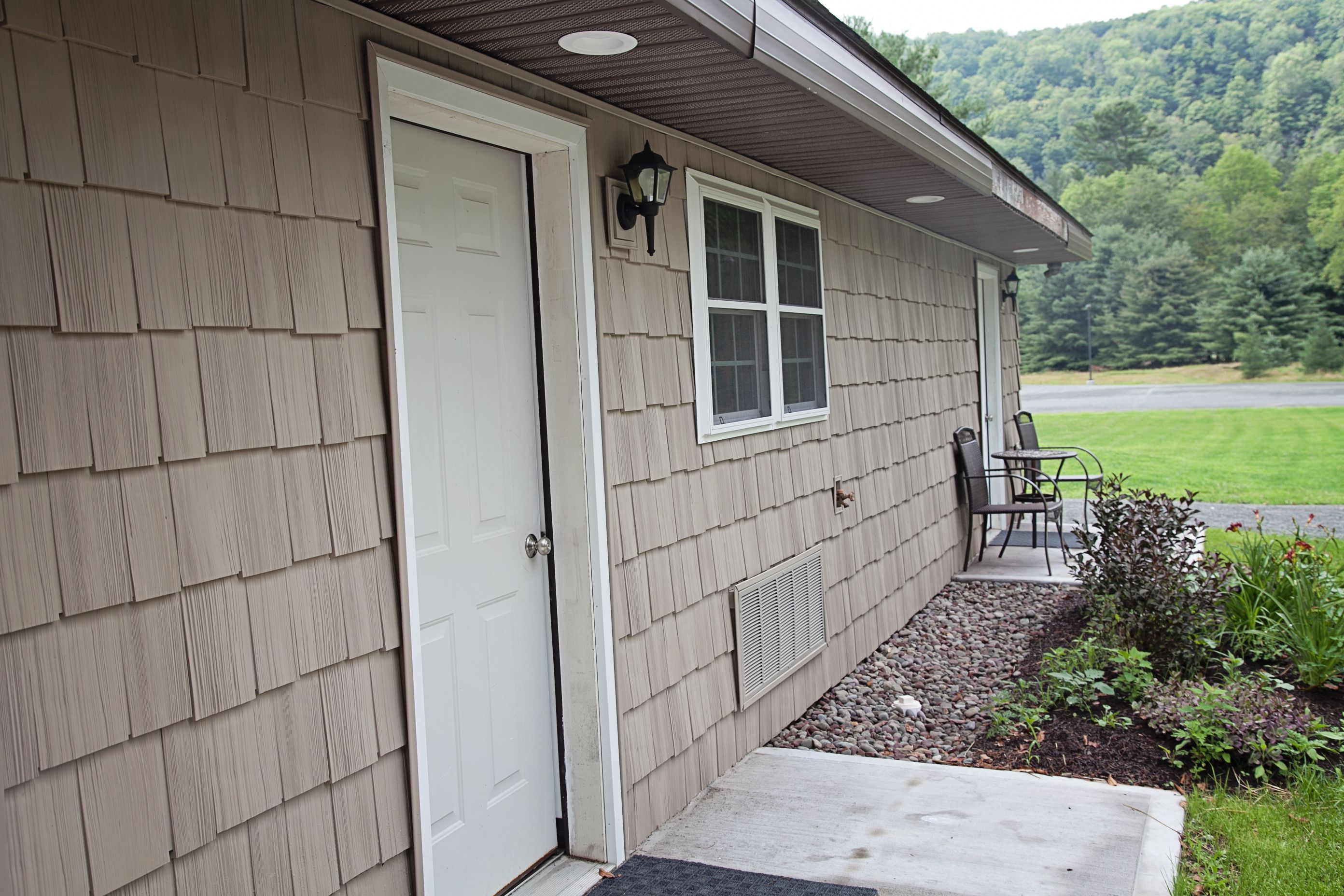A house with a front door, a window, a porch with a chair, and a small garden area.