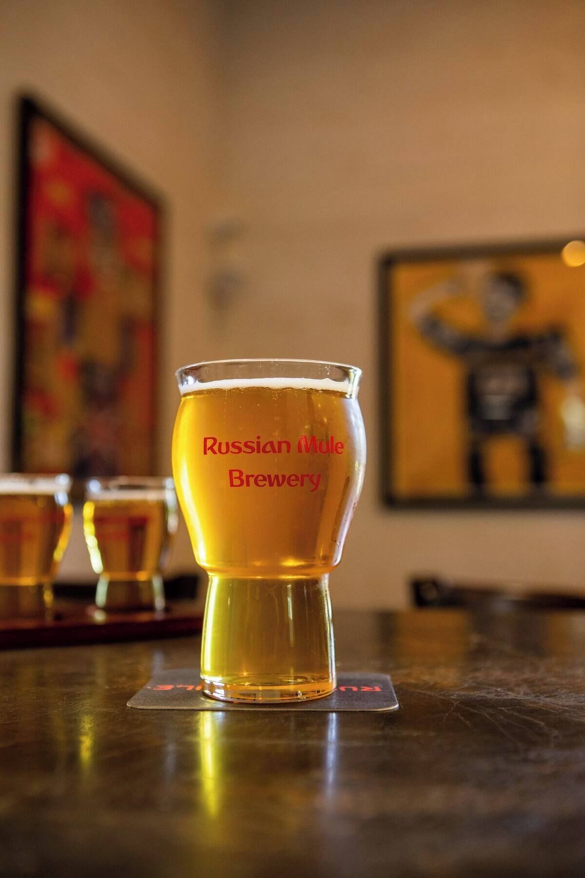 A glass of beer with "Russian Mule Brewery" written on it, placed on a coaster.
