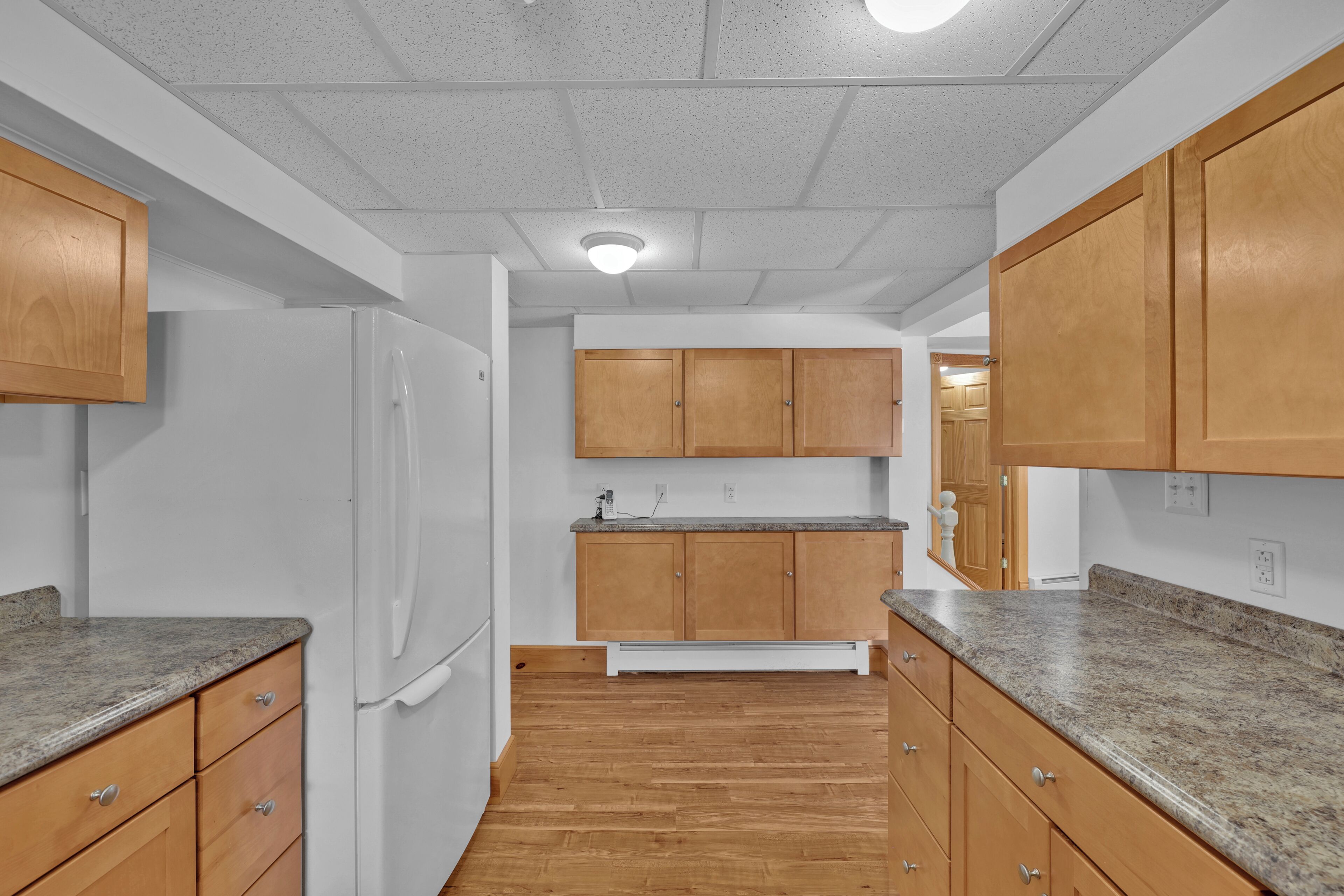 A kitchen with wooden cabinets, granite countertops, and a white refrigerator.