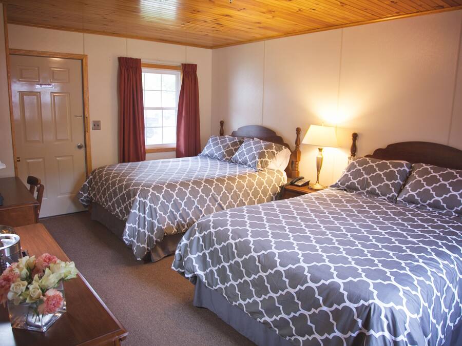 A hotel room with two beds, a desk with a lamp, and a window with curtains.