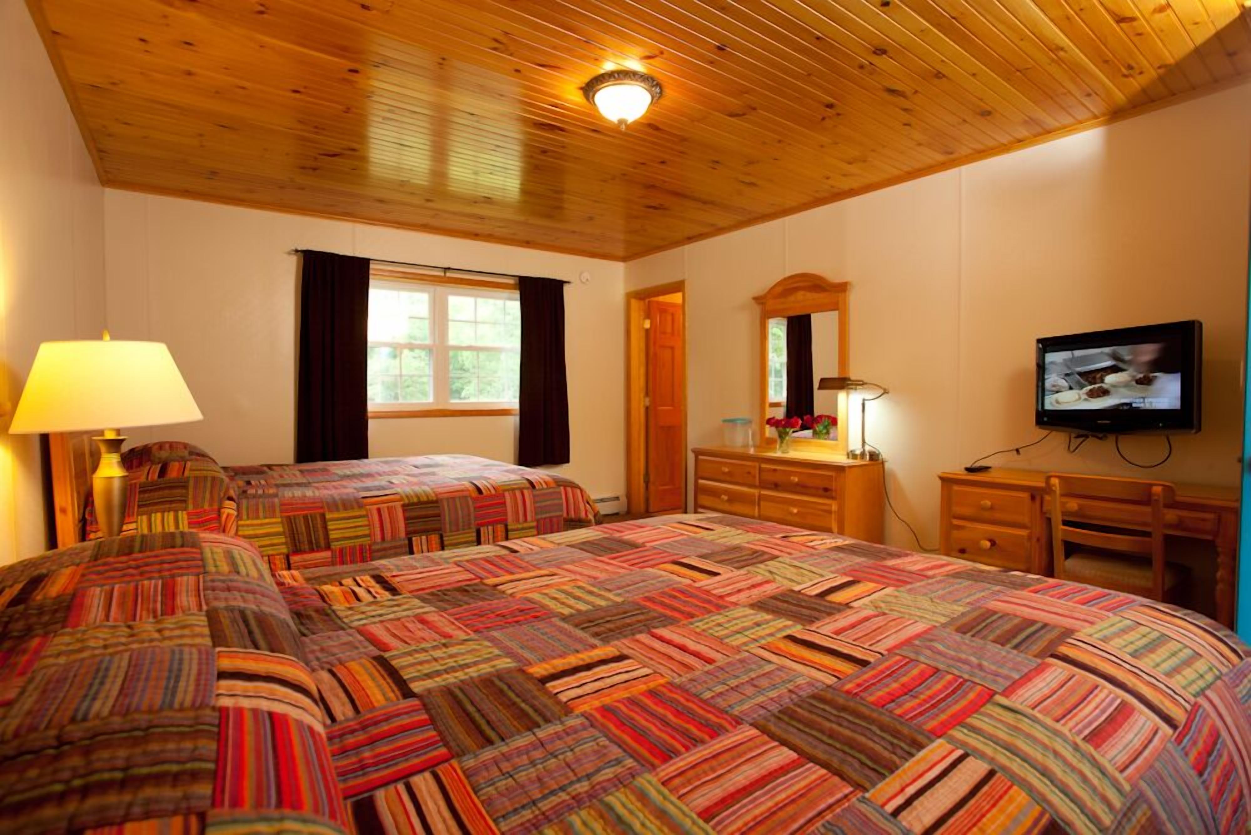 A bedroom with a large bed, two bedside tables, a dresser, a television, and a window with curtains.