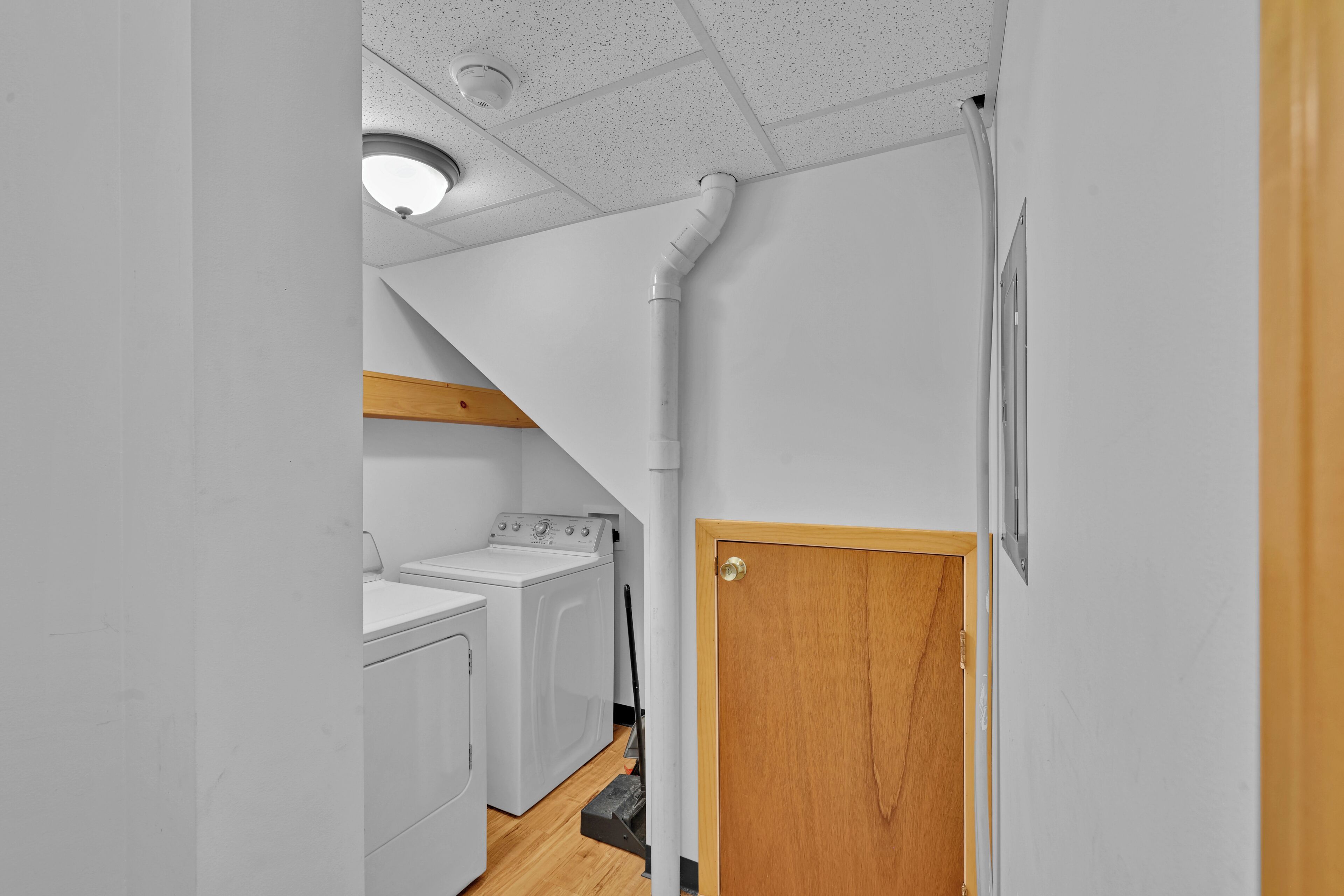 A laundry room with a washing machine and dryer, a wooden beam ceiling, and a door with a wooden frame.
