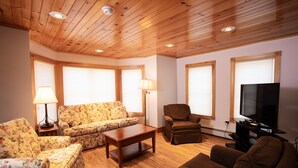 A living room with wooden flooring, a sofa, a chair, a coffee table, and a television. - Blue Hill Lodge (Claryville)