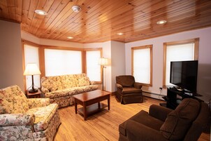 Una sala de estar con piso de madera, un sofá, un sillón, una mesa de centro y un televisor.