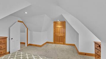 Een slaapkamer met een schuine plafond, een houten deur, een dressoir en een bed met een gestreept laken.