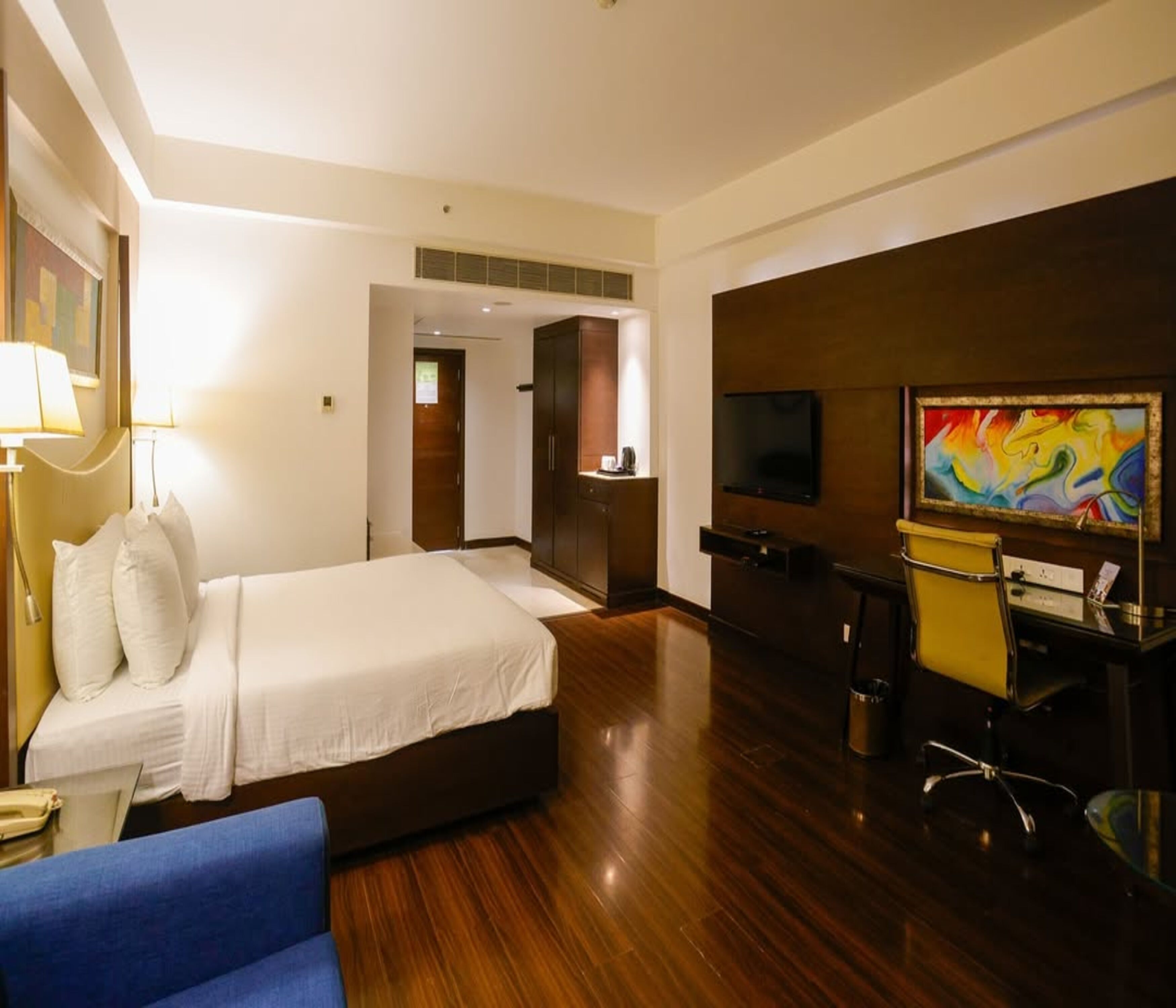 Een hotelkamer met een bed, een bureau met stoel, een televisie en een schilderij aan de muur.