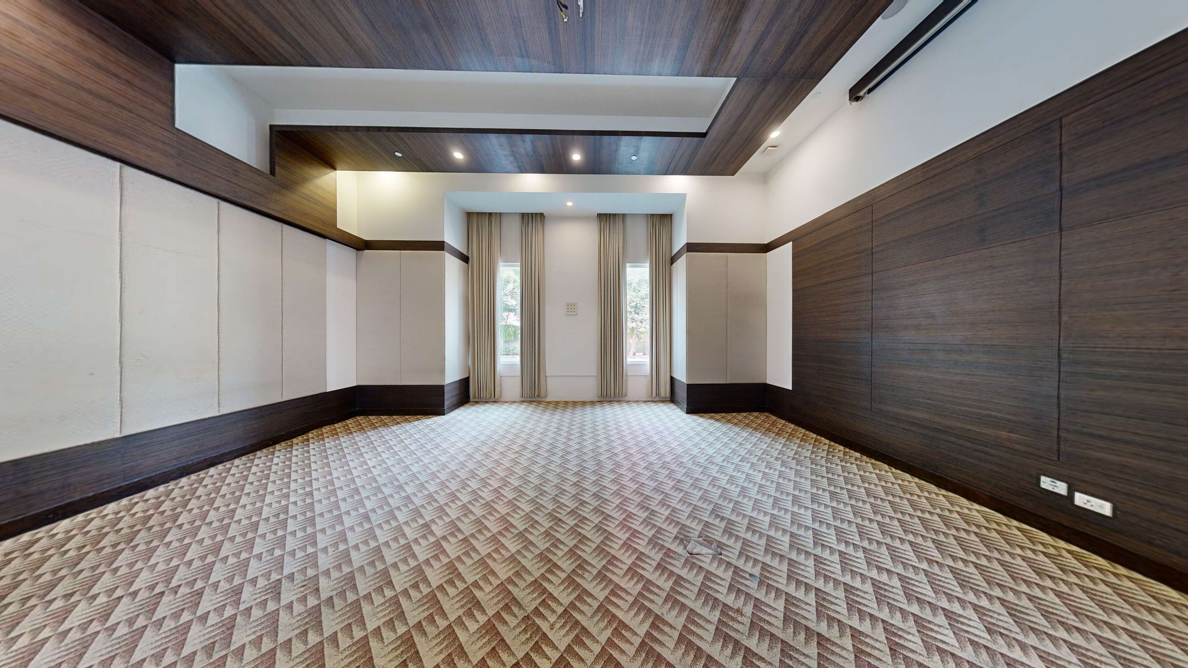 A spacious room with a patterned carpet, wooden panel walls, and a ceiling with recessed lighting.