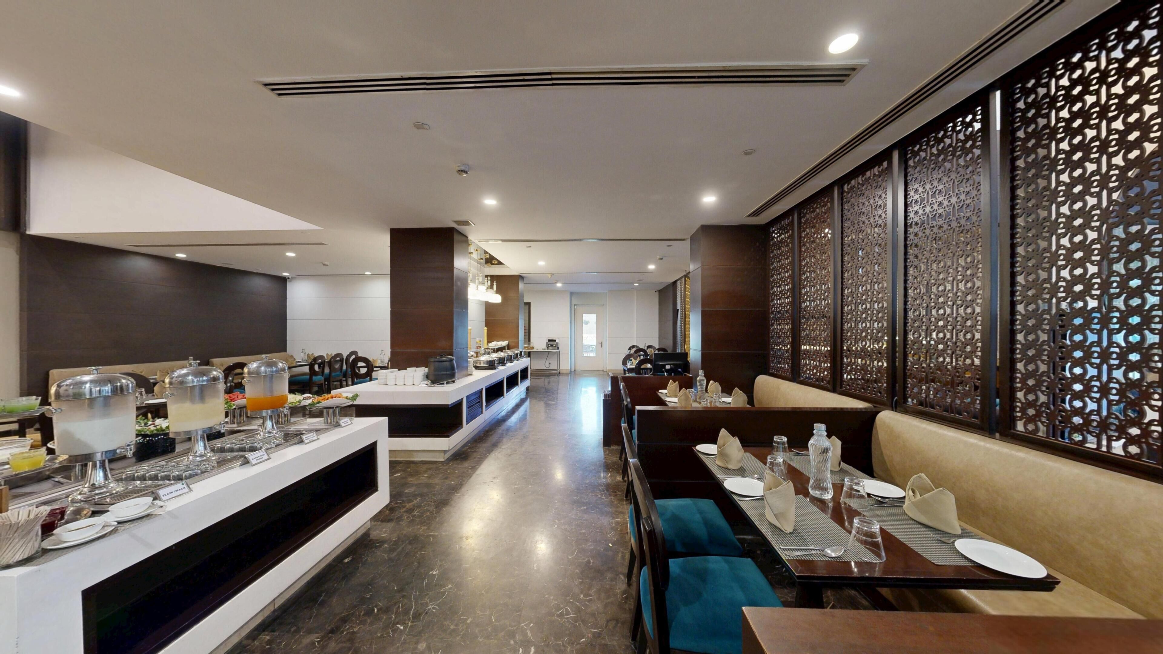 Comedor moderno de hotel con mostradores tipo buffet, disposición de mesas y paneles decorativos en las paredes.