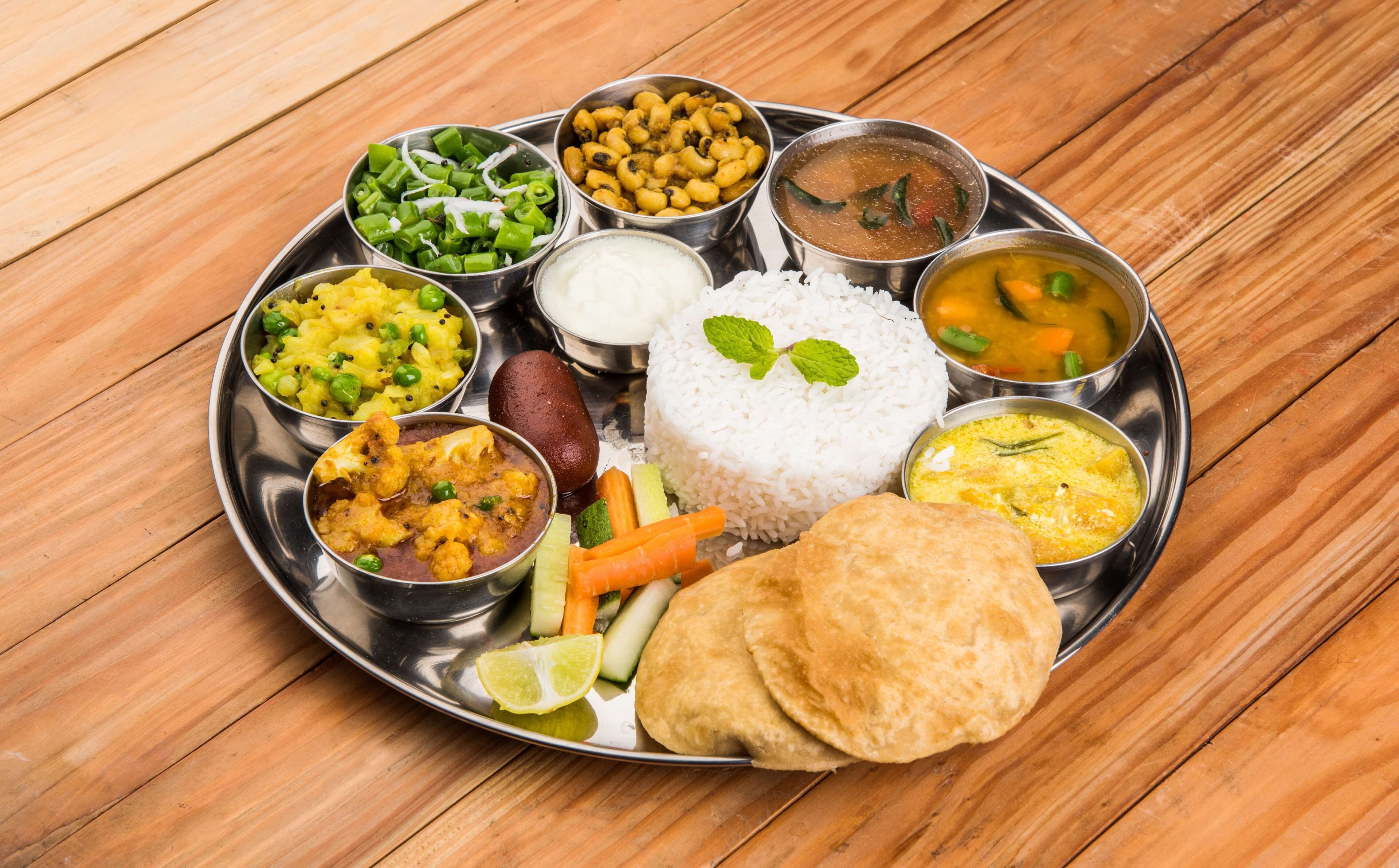 Un repas traditionnel indien servi dans une assiette en acier inoxydable, accompagné de différents plats, notamment du riz, un curry et des légumes.