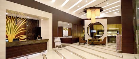 Um saguão de hotel com balcão de recepção, área de estar e um espelho grande.