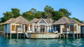 Overwater bungalows with thatched roofs, wooden walkways, and clear blue water. - SONG SAA PRIVATE ISLAND (Koh Ouen)