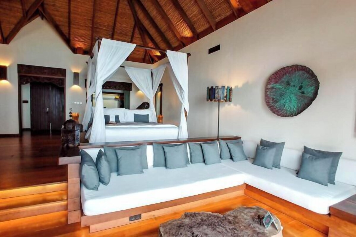 A room with a large white sofa, a canopy bed, wooden flooring, and a decorative wall piece.