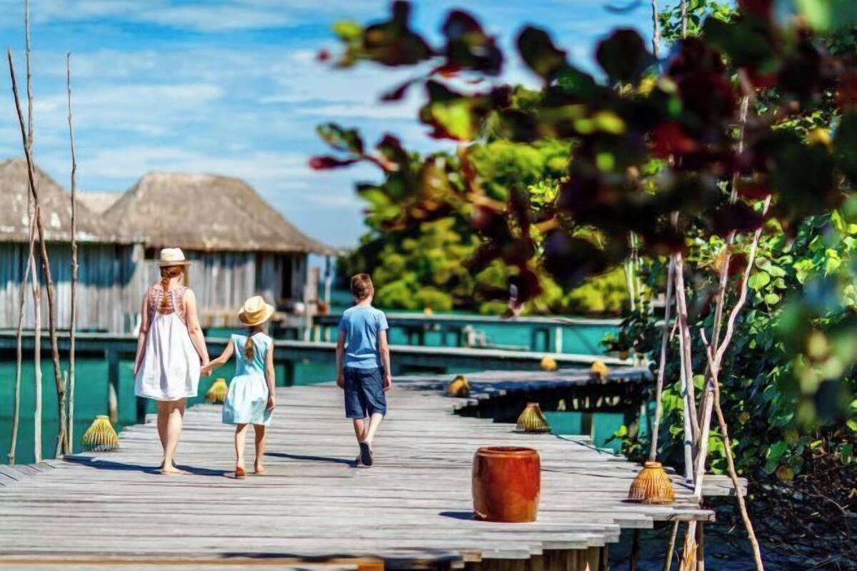 Un muelle de madera que se adentra en un cuerpo de agua, con bungalows sobre el agua al fondo.