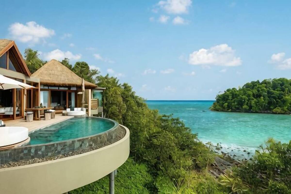 Un resort con piscina infinita privada, una estructura de techo de paja y vista al océano y una pequeña isla.