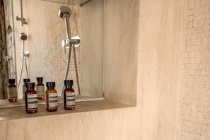 Un baño con ducha, un espejo y varias botellas de champú sobre el lavamanos.