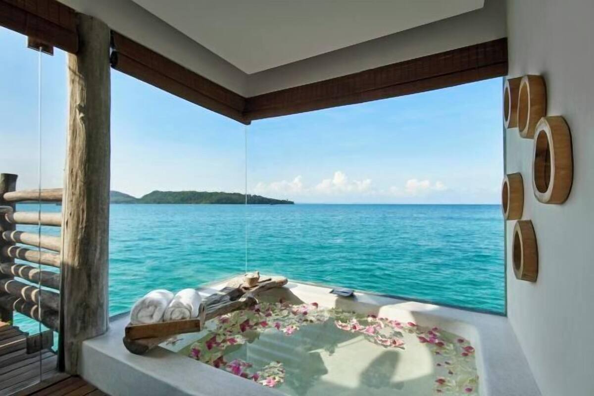 Un balcón con vista al mar, una terraza de madera y una bañera con toallas y flores.