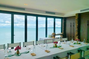 A dining area with a view of the sea, large windows, and a long table set for a meal. - SONG SAA PRIVATE ISLAND (Koh Ouen)