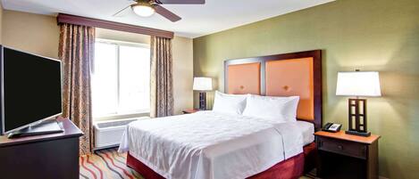 A hotel room with a bed, a TV, a desk, a chair, a lamp, and a ceiling fan.