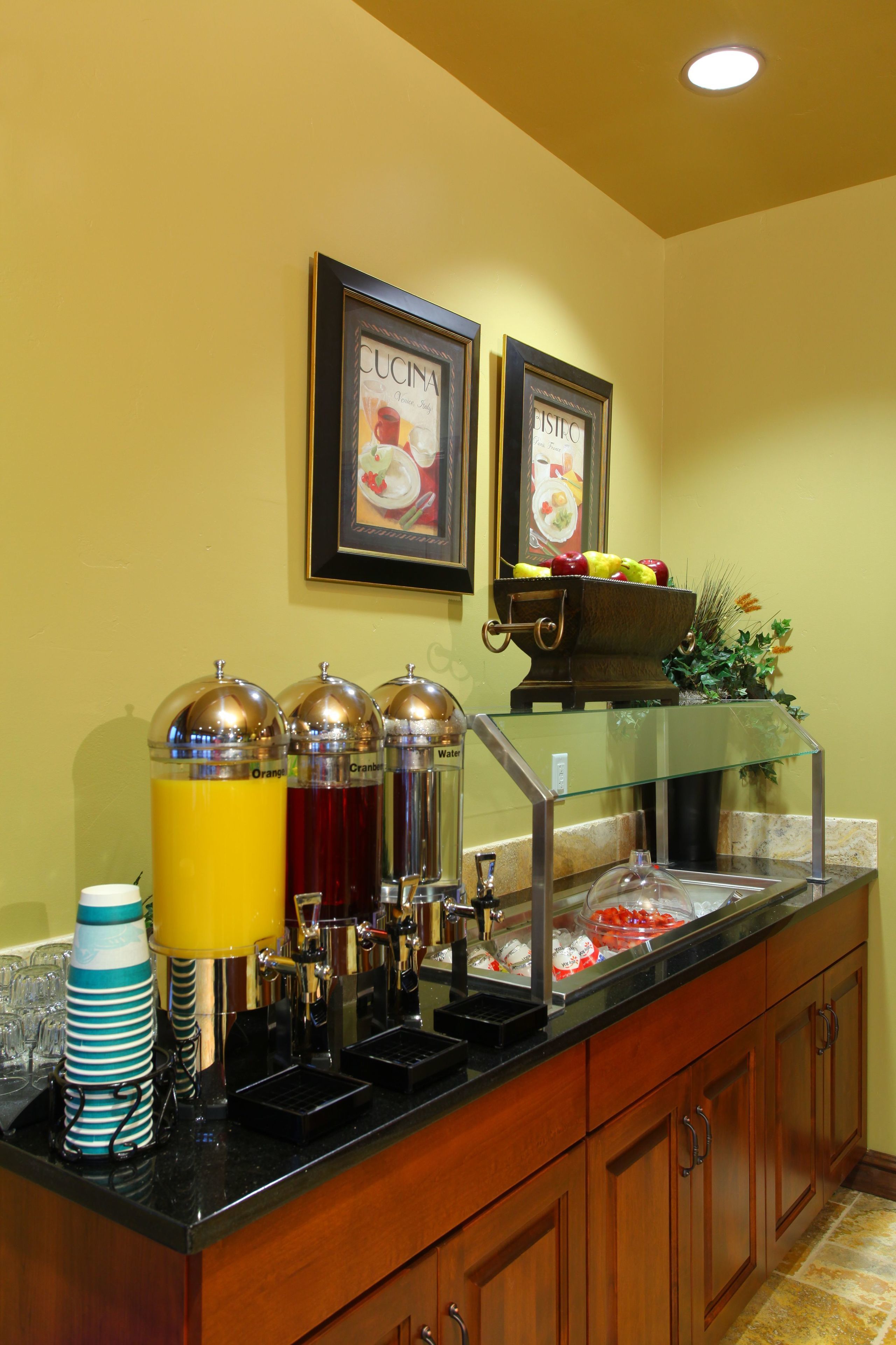 A buffet area with a glass display case, fruit bowl, and beverage dispensers.