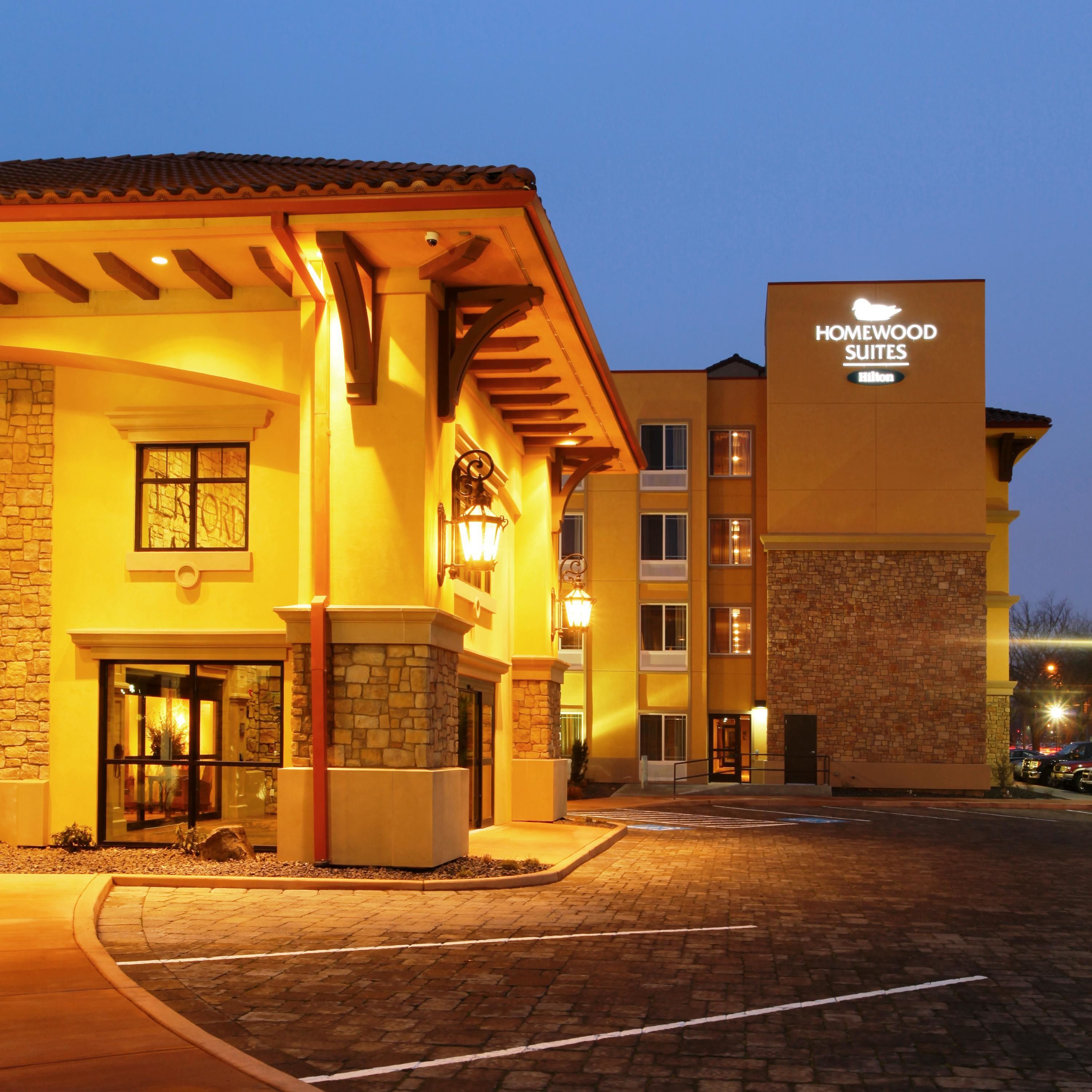 A hotel with a stone facade, a sign for Homewood Suites, and a brick-paved entrance.