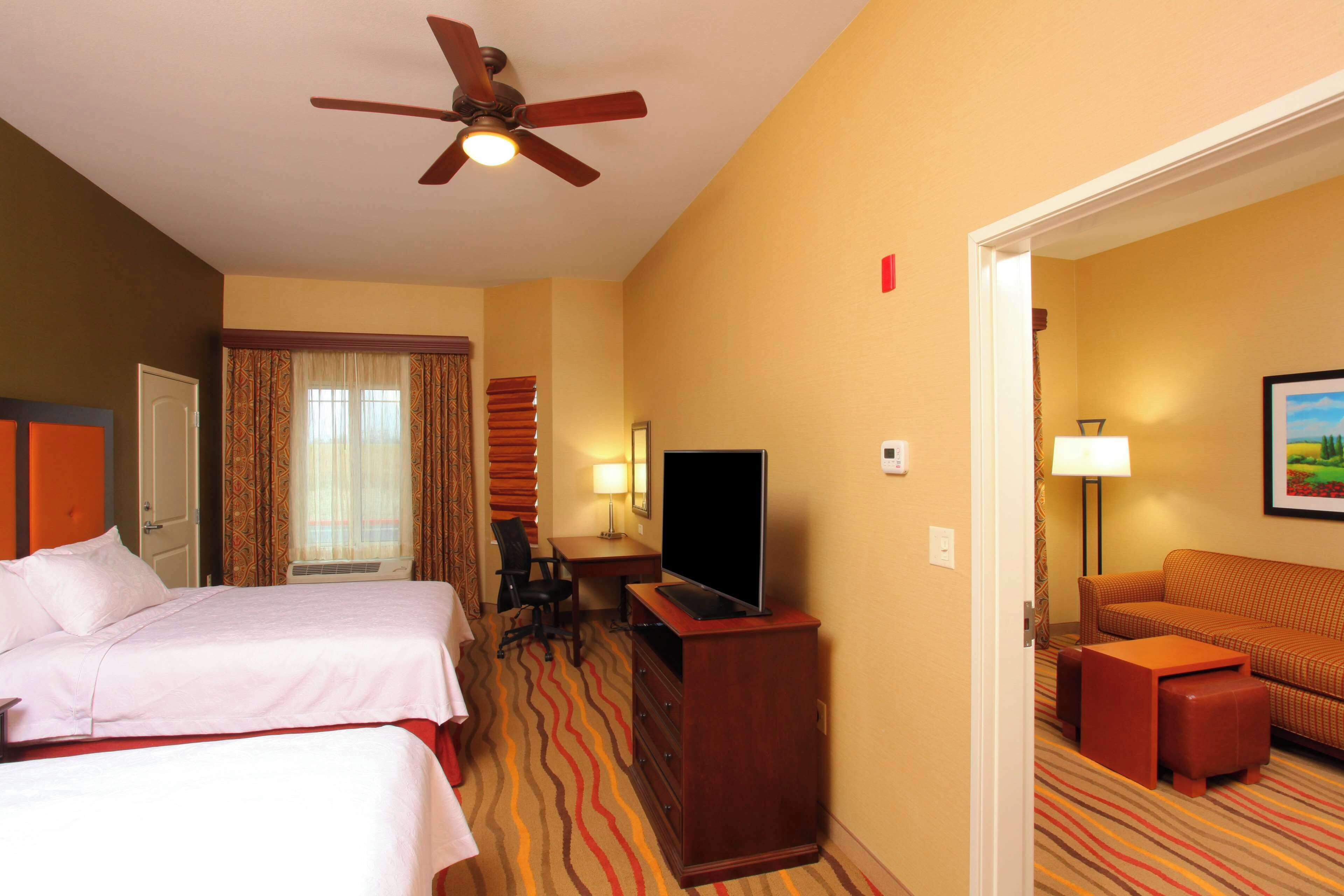 A hotel room with two beds, a desk with a TV, a sofa, and a ceiling fan.