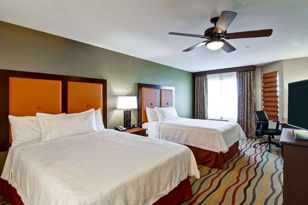 Une chambre d’hôtel avec deux lits, un ventilateur de plafond, un bureau et une télévision.