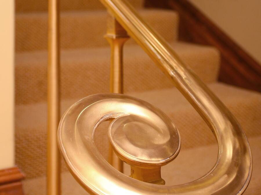 A spiral staircase with a golden handrail and beige carpeted steps.