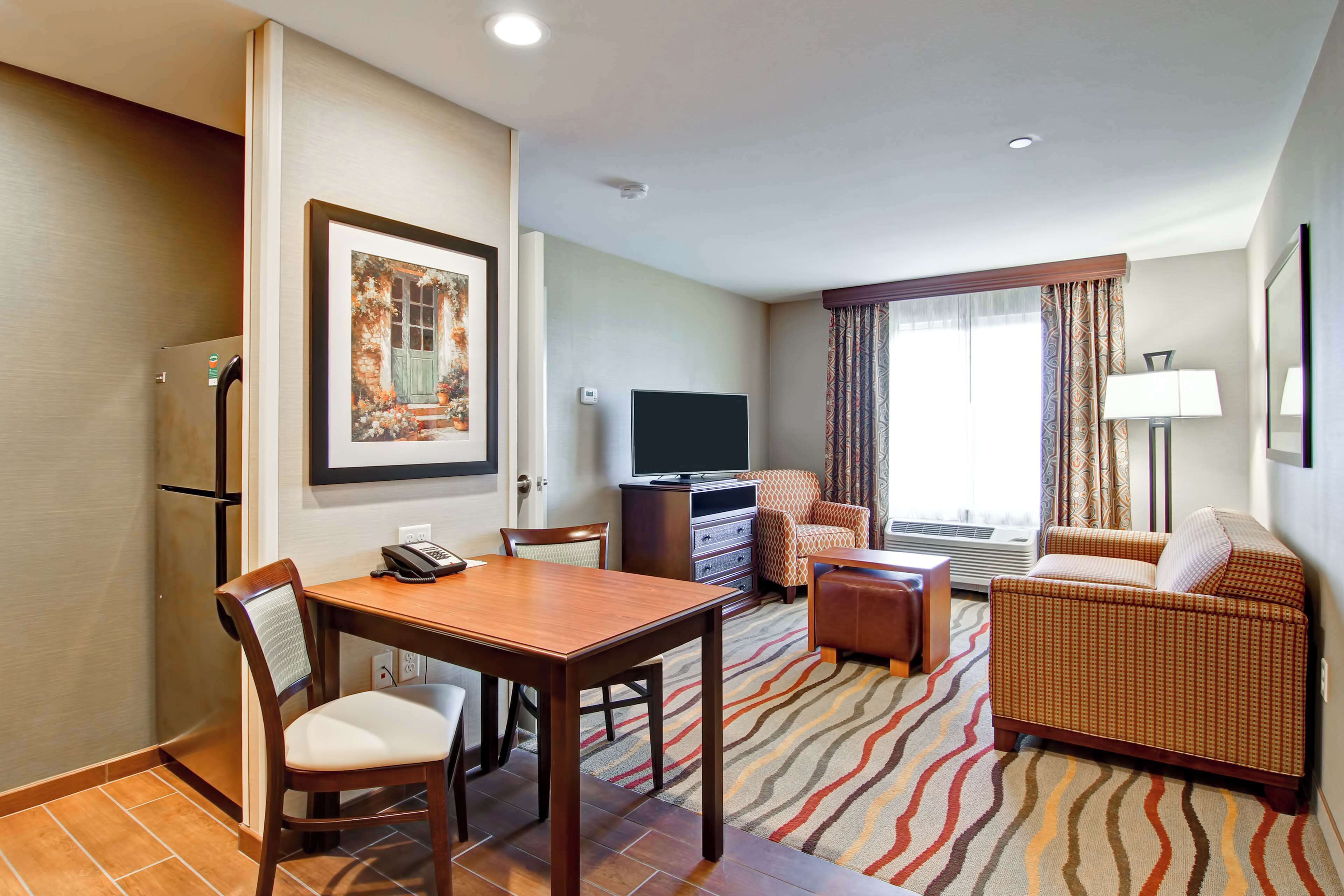 A hotel room with a dining table, chairs, a sofa, a TV, and a patterned rug.