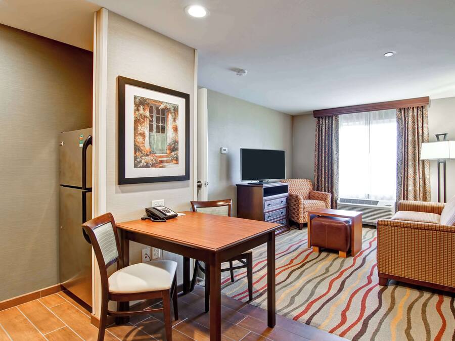 A hotel room with a dining table, chairs, a sofa, a TV, and a patterned rug.