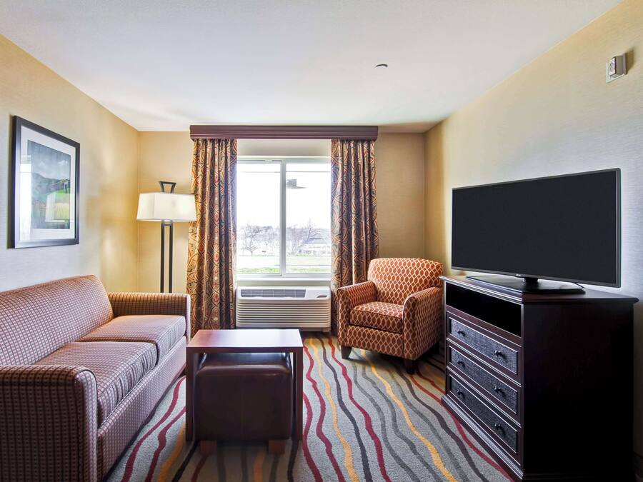 Quarto de hotel com sofá, poltrona, televisão e vista para o exterior pela janela.