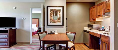 A modern kitchen with wooden cabinets, a microwave, and a dishwasher. There is a dining table with chairs and a framed picture on the wall.
