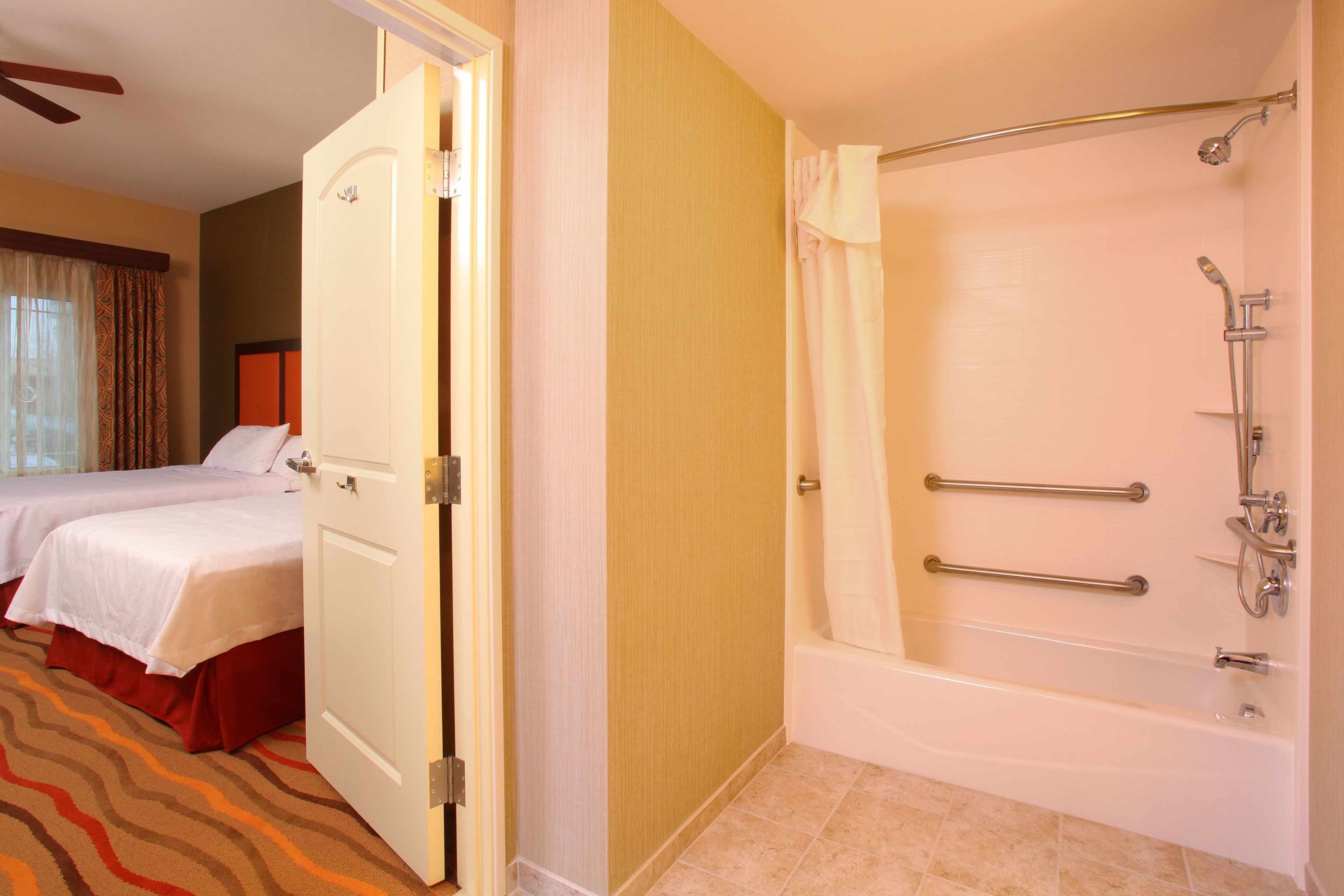 A hotel room with two beds, a bathtub with grab bars, and a door leading to another room.
