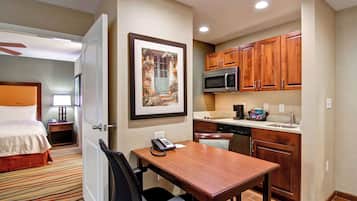 A hotel room with a bed, a desk with a telephone, a microwave, and wooden cabinets.