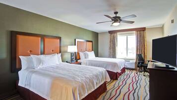 A hotel room with two beds, a ceiling fan, a TV, and a window with curtains.