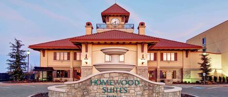 Un hôtel à la façade en pierre, doté d’une tour horlogée et d’une enseigne indiquant « HOMEWOOD SUITES Hilton ».
