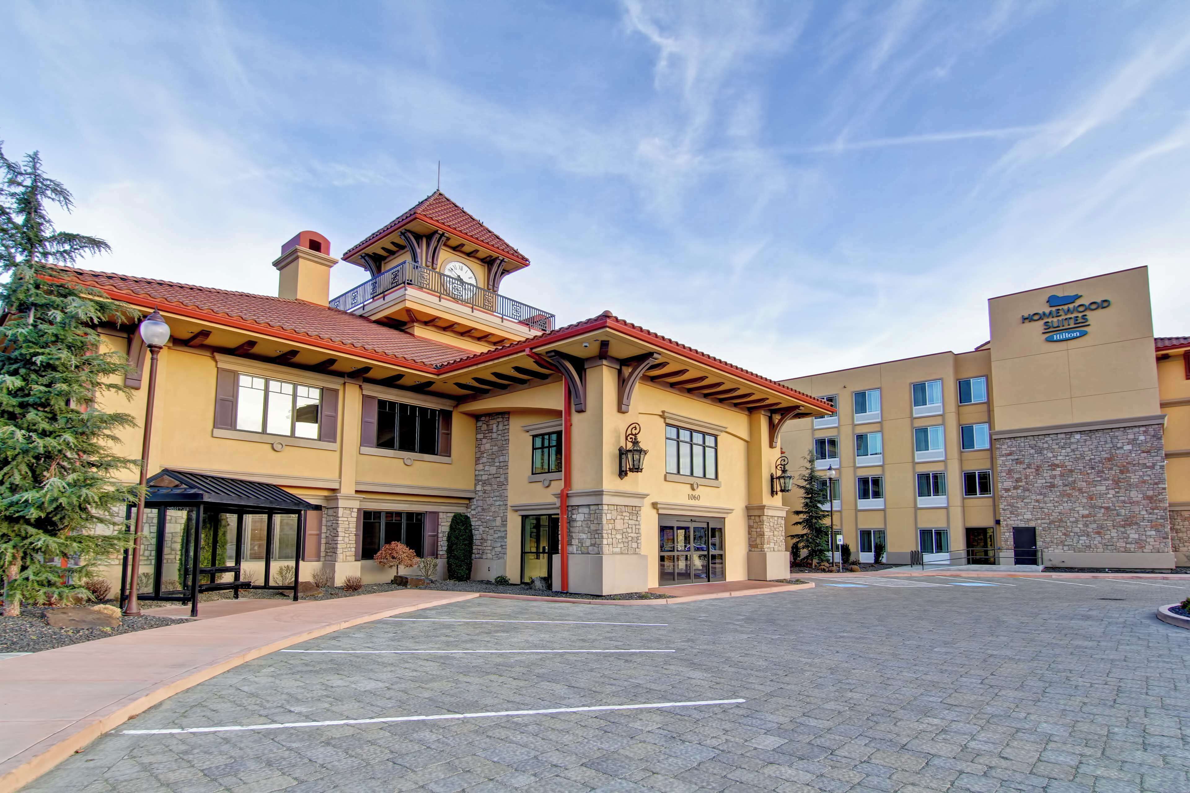 Un hotel con un patio central, una zona de estar cubierta y una entrada destacada con un campanario.