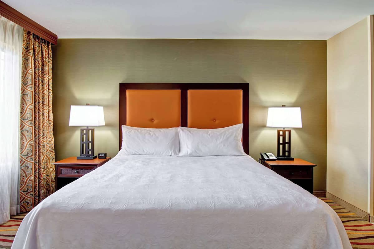 Une chambre d’hôtel avec un grand lit, deux tables de chevet avec des lampes et un rideau à motifs.