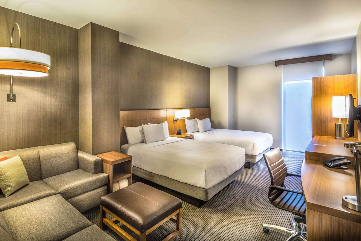 A hotel room with two beds, a sofa, a desk, and a chair.