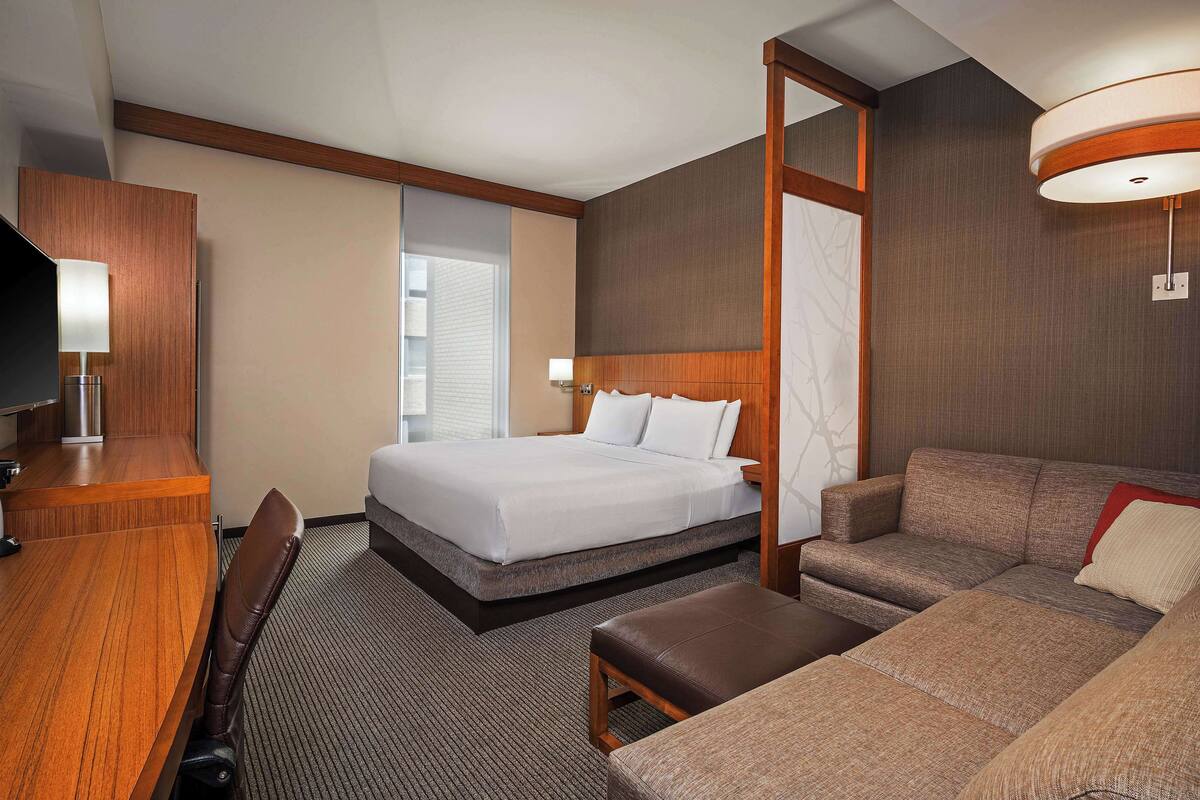 A hotel room with a bed, a sofa, a desk, and a television.