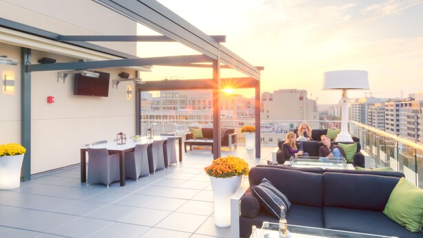 Une terrasse sur le toit avec des sièges en plein air, un espace bar et une vue imprenable sur le coucher de soleil.